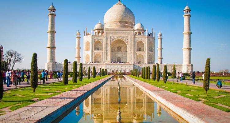 The iconic white marble Taj Mahal reflected perfectly in its long central pool under a clear blue sky.