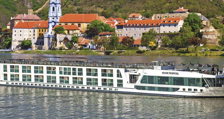 Moderne witte riviercruiseschip vaart langs de blauw-getorende kerk en kleurrijke dorp Dürnstein aan de Donau.