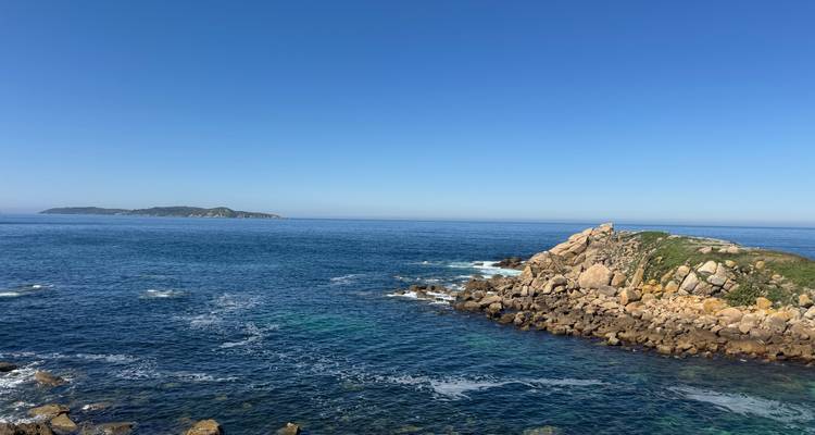 Heldere blauwe oceaan die een rotsachtige kaap omringt met een ver eiland aan de horizon