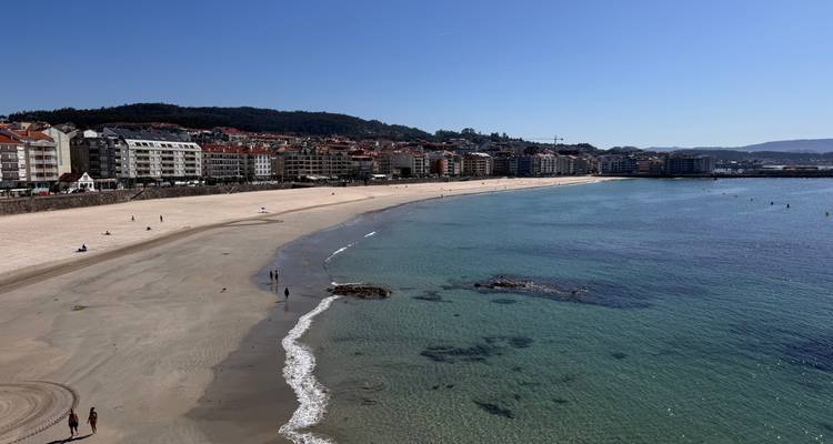 Breed zandstrand dat zich langs een kuststad kronkelt met zwemmers en zonnebaders