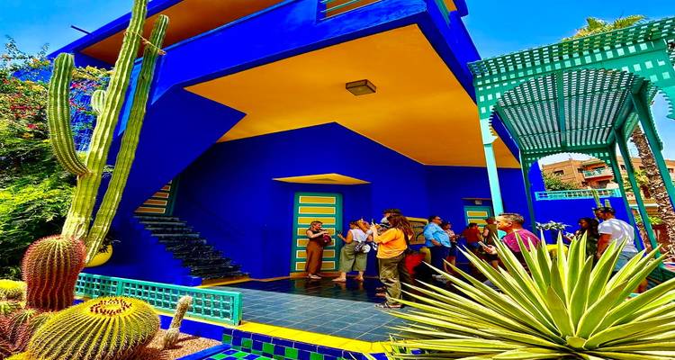 Tour group visiting vivid blue and yellow Art Deco building surrounded by cacti