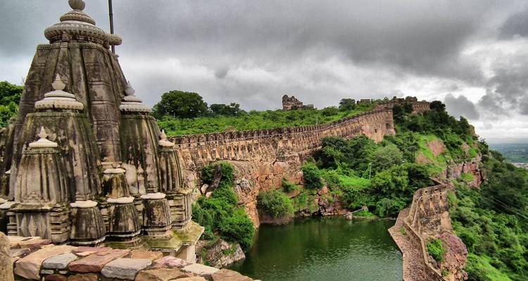 Murs expansifs du fort de Chittorgarh et temple surplombant les douves vertes par une journée nuageuse.