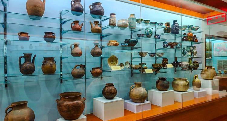 Vitrine du musée de verre avec des rangées de poteries et de céramiques anciennes dans des vitrines bien éclairées.