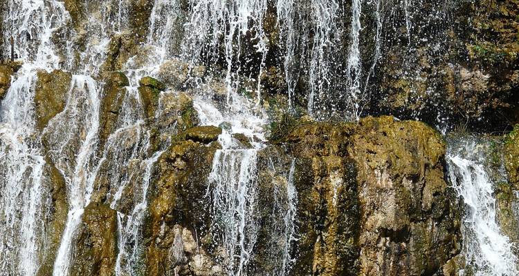 Close-up zicht op water dat over bemoste rotsformaties van een natuurlijke waterval stroomt.