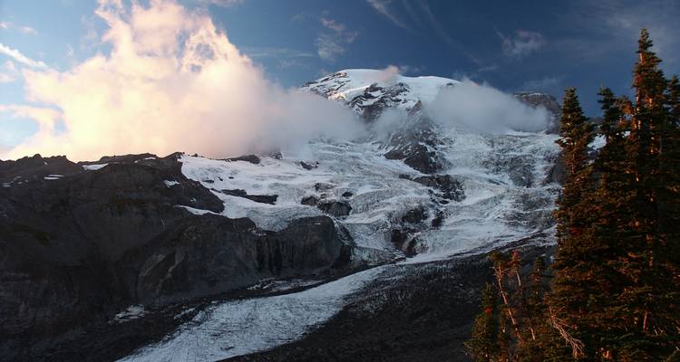 Gegletserd gezicht van Mount Rainier verlicht door de late middagzon met slierten wolk die aan de top kleven.