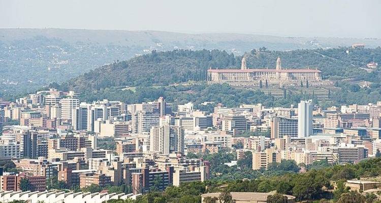 Elevated panorama of a sprawling South African city backed by a low green ridge and Union Buildings.