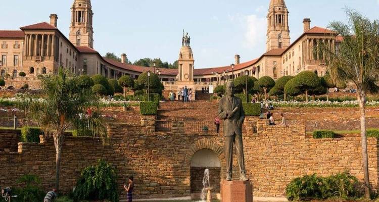 Stately sandstone Union Buildings with tiered gardens and central statue under a clear sky.