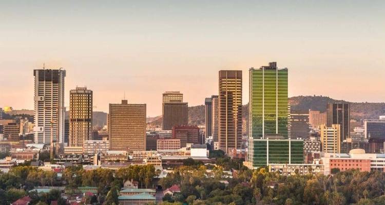 Modern skyline of a South African city glowing in warm sunset light with hills in the background.