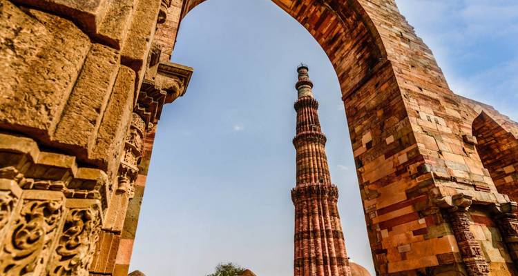 Qutub Minar bekeken door sierlijke stenen boogdoorgangen tegen een heldere hemel.