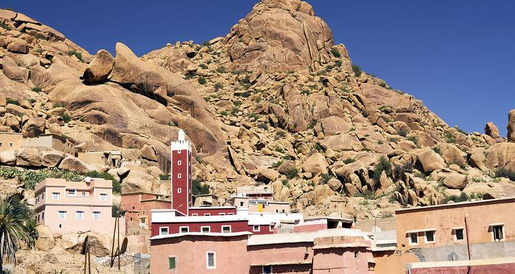 Traditionele roze en rode dorpshuizen en een hoge minaret genesteld onder ruige granieten heuvels in Tafraoute.