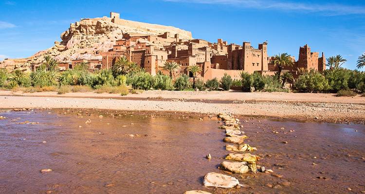 Kasbah de barro de la UNESCO de Ait Benhaddou encaramada en la cima de una colina sobre un lecho de río seco con piedras de paso.