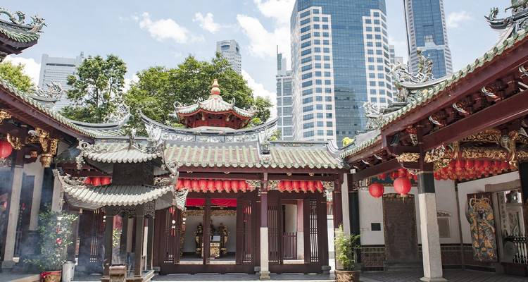 Cour de temple chinois traditionnel à Singapour encadrée par des toits ornés avec des gratte-ciel modernes au-delà.