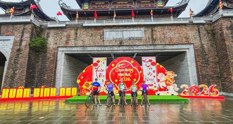 Cycling group poses with bikes before a festive Vietnamese temple gate adorned with New Year 2026 decorations.