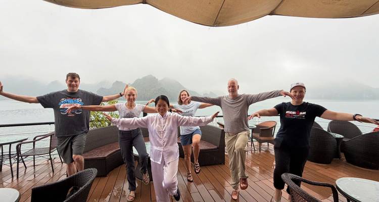 Travelers practice balancing exercises on a cruise deck with misty limestone karsts of Halong Bay behind.