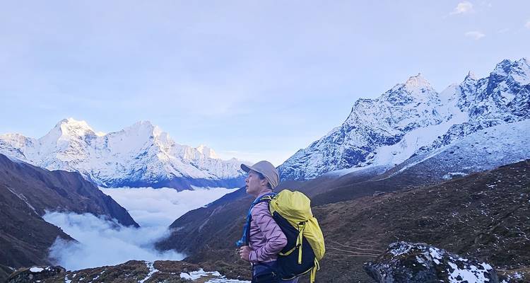 Vrouwelijke trekker met een gele rugzak staart naar dramatische, met sneeuw bedekte Himalaya-toppen boven een wolkeninversie.