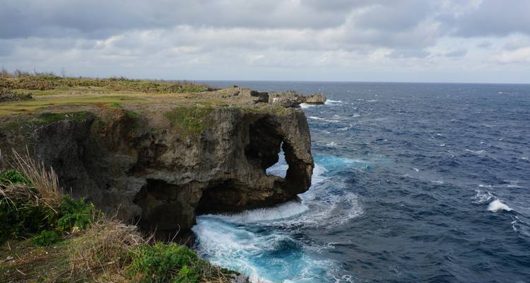 Rugged coastal cliff resembling an elephant trunk jutting into deep blue seas with crashing surf in Okinawa.