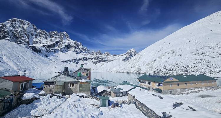 Snow-covered mountain village beside an icy lake under a deep blue alpine sky.