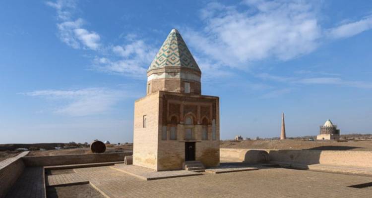Vierkant mausoleum met gedessineerd dak op een betegeld terras onder blauwe luchten.