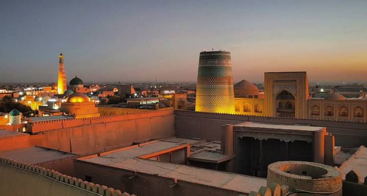 Panoramische zonsondergang over Khiva's ommuurde stad met verlichte minaretten en koepels.