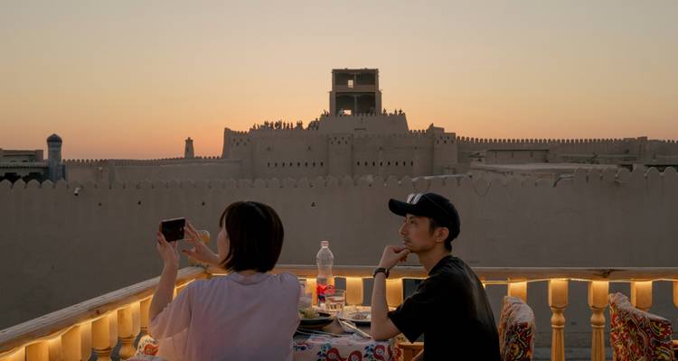 Stel dineert op een dakterras bij zonsondergang met uitzicht op Khiva's lemen muren.