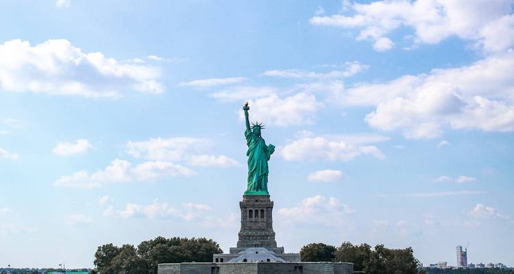 La Estatua de la Libertad erguida contra un cielo azul salpicado de nubes.