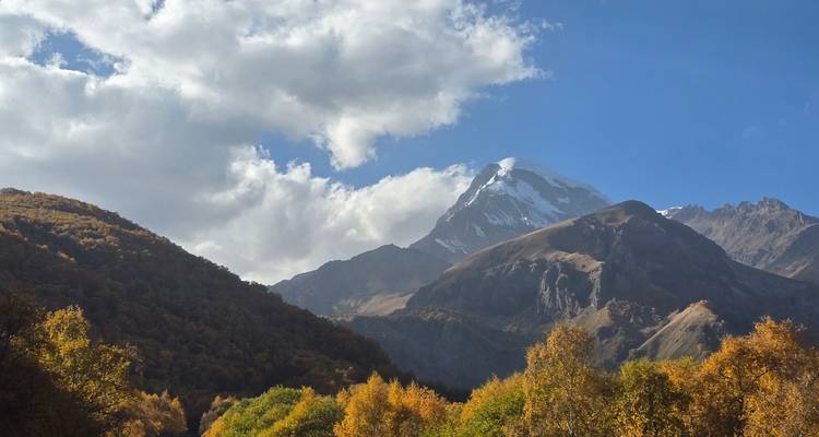 De top van de berg Kazbek rijst op boven de herfstgekleurde valleien onder dramatische wolken.