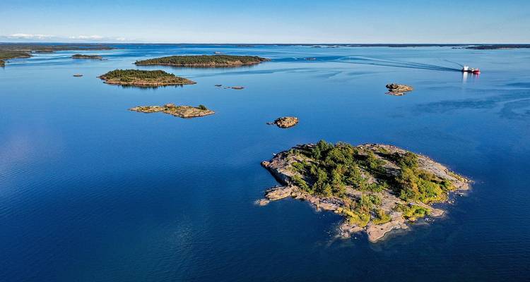 Aerial view of scattered green islets and deep blue ocean with small ferry leaving wake