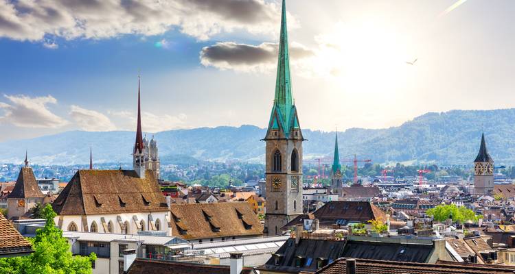 Panoramic view of Zurich old town rooftops and tall church spires against alpine backdrop