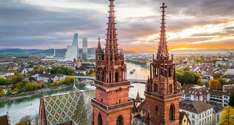 Luftaufnahme der Doppeltürme des Basler Münsters mit gemusterten Dachziegeln mit Blick auf den Rhein bei Sonnenuntergang