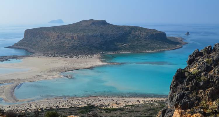 Panoramisch uitzicht op een turquoise lagune en klein eilandplateau omringd door diepblauwe zee, gezien vanaf een rotsachtige klif.