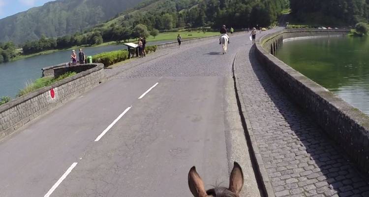 View from horseback riding across a cobblestone bridge with green hills and lake beyond.