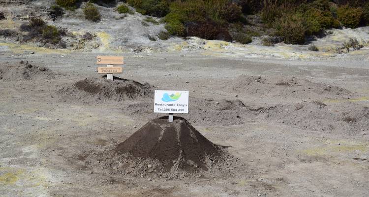 Conical sand mounds marking underground stew cooking sites with restaurant sign