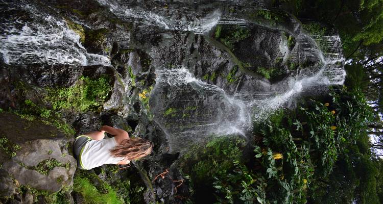 Multi-tiered jungle waterfall with traveller seated on rock admiring the scene