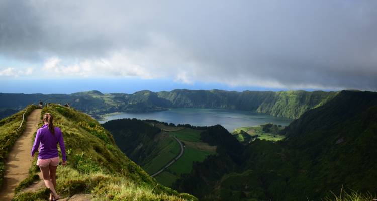 Hiker walking along a scenic ridge overlooking the twin lake caldera with lush green cliffs under dramatic clouds