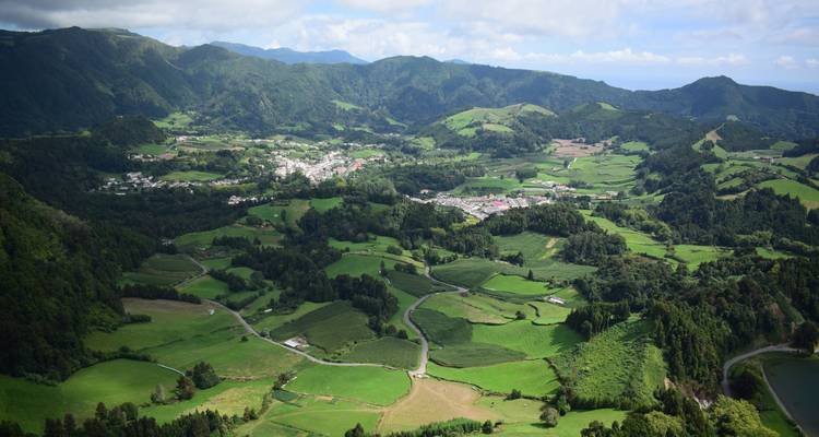 Expansive aerial view of green valleys, villages, and distant hills under light clouds