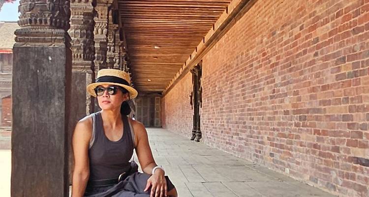 Portrait of a seated woman in a historic brick corridor wearing hat and sunglasses