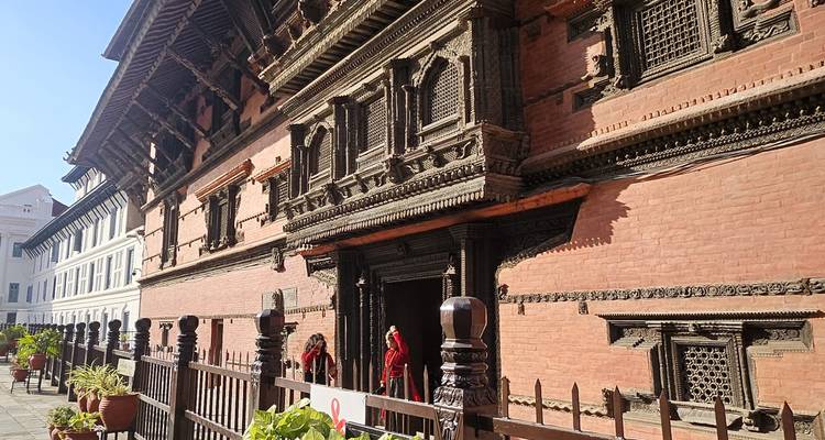 Two women in red saris stand outside an intricately carved brick palace façade