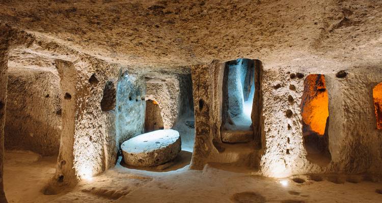 Beleuchtete Kammern einer unterirdischen Stadt, die in Vulkangestein gehauen wurde, mit rauen Steinwänden und runden Türöffnungen