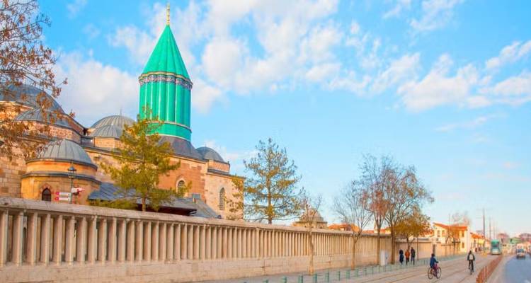 Außenansicht des Mevlana-Museums mit seiner charakteristischen grünen kegelförmigen Kuppel und einer freien Fußgängerzone in Konya