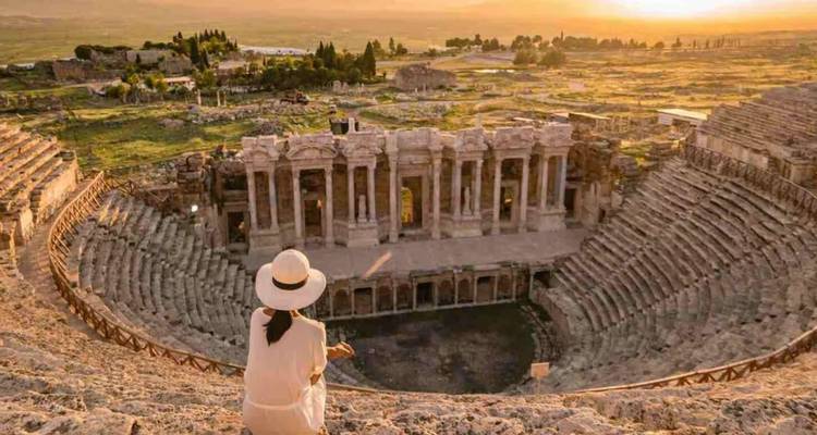 Weibliche Reisende in weißem Kleid und Hut blickt auf das große römische Theater in Hierapolis während des goldenen Sonnenuntergangs