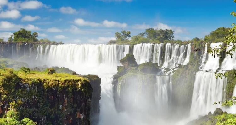 Large panorama des chutes d'Iguazu cascadant par-dessus des falaises luxuriantes sous un ciel dégagé