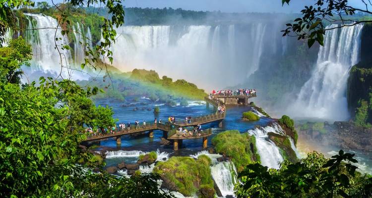 Vue en plongée de la passerelle courbe avec des visiteurs et arc-en-ciel se formant dans les embruns d'Iguazu
