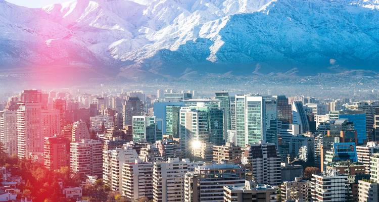 Moderno horizonte de rascacielos bajo dramáticos picos nevados de los Andes con un destello de lente de luz rosa.