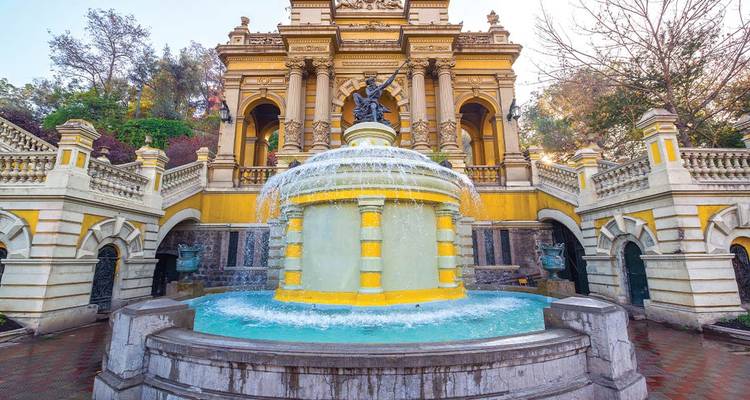 Fuente neoclásica amarillo brillante salpica agua frente a una escalinata ornamentada y arcos.