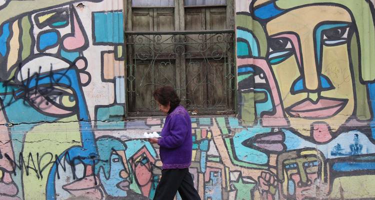 Una persona camina frente a un mural de arte callejero vibrante que presenta rostros abstractos y colores llamativos.