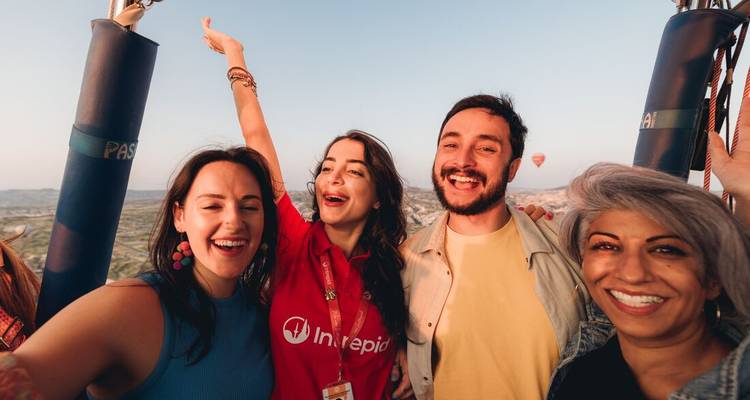 Aufgeregte Reisende lächeln in einem Heißluftballonkorb mit Kappadokiens Landschaften, die unten sichtbar sind.