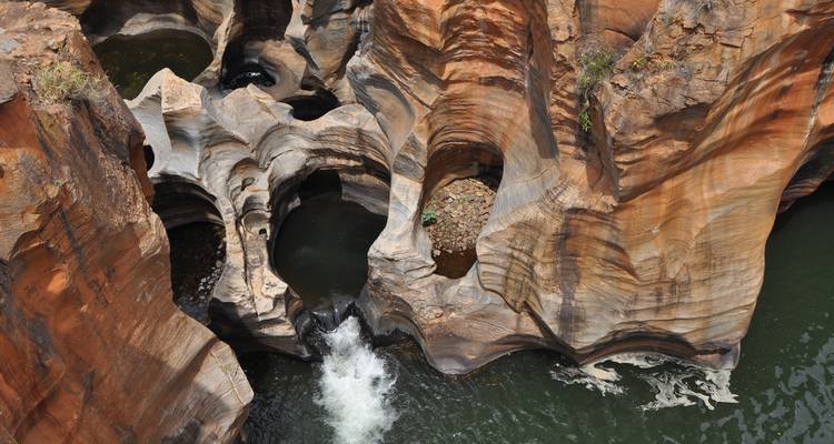 Vue aérienne de formations spectaculaires de marmites cylindriques creusées dans du grès rouge avec de l'eau qui coule rapidement.