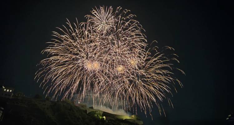 Brilliant burst of fireworks illuminating the night sky above a fortress hillside.