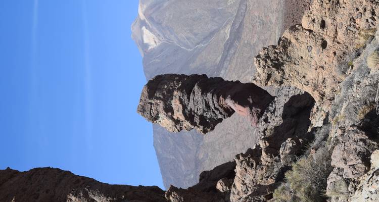 Iconic Roque Cinchado rock pillar with Mount Teide snow patch in background under clear sky