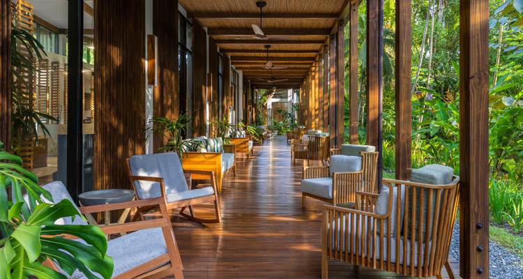 Long wooden veranda lined with cushioned chairs looking onto tropical gardens.